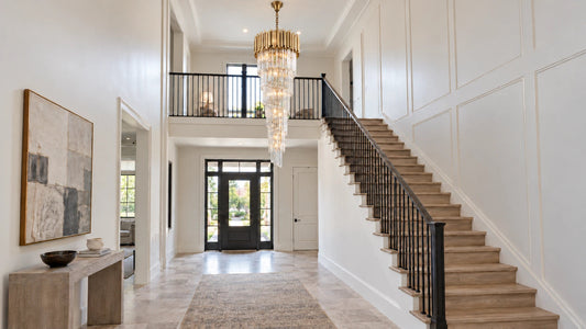 A tapered crystal chandelier with a brass tube crown hangs in a two-story foyer beside an oak staircase.
